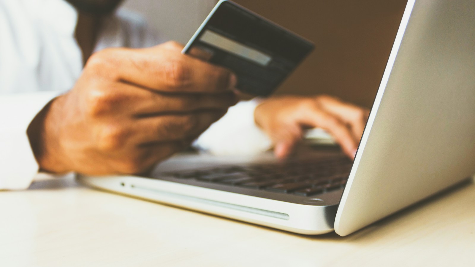 Pessoa segurando cartão de crédito enquanto compra pelo notebook
