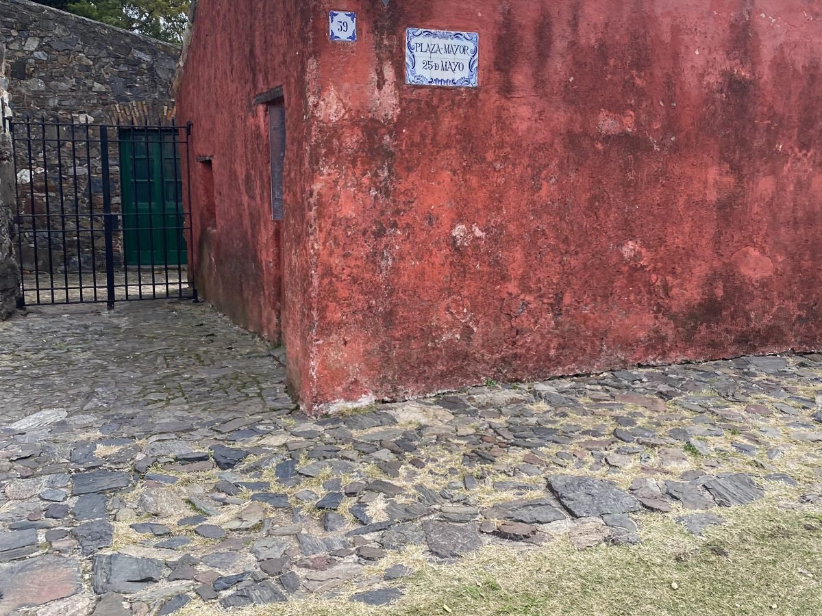 Casa colonial vermelha com placa de azulejo da Plaza Mayor 25 de Mayo, em Colônia do Sacramento