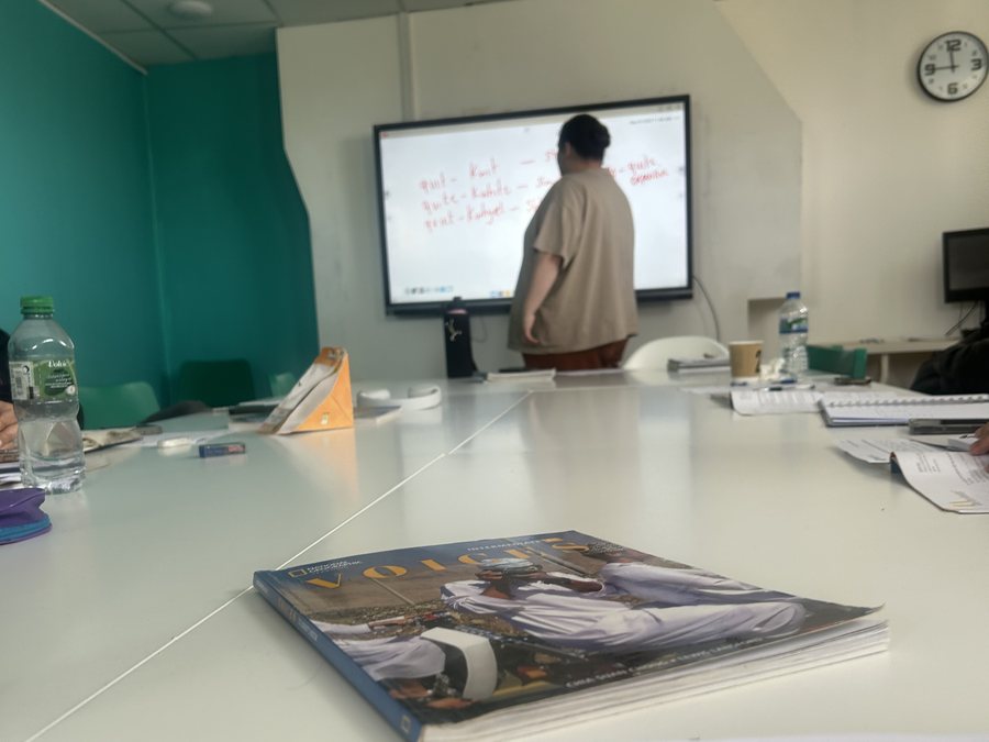 Sala de aula da escola de inglês em Liverpool, com livro sobre a mesa e professora na lousa digital