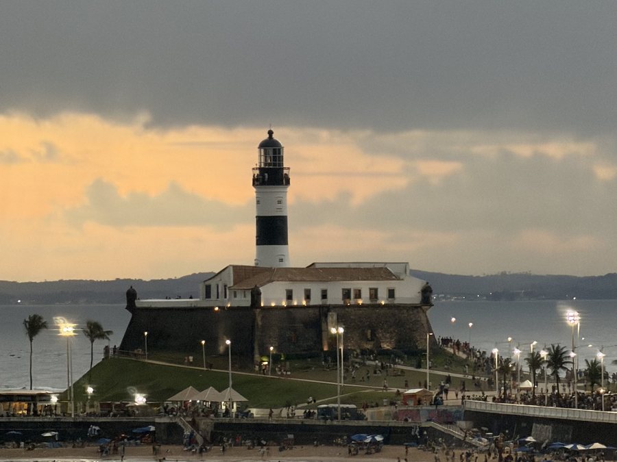 Farol da Barra ao entardecer, com o céu dourado e a orla iluminada