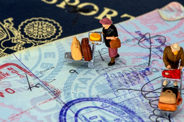 Miniaturas de viajantes com malas sobre página de passaporte carimbada